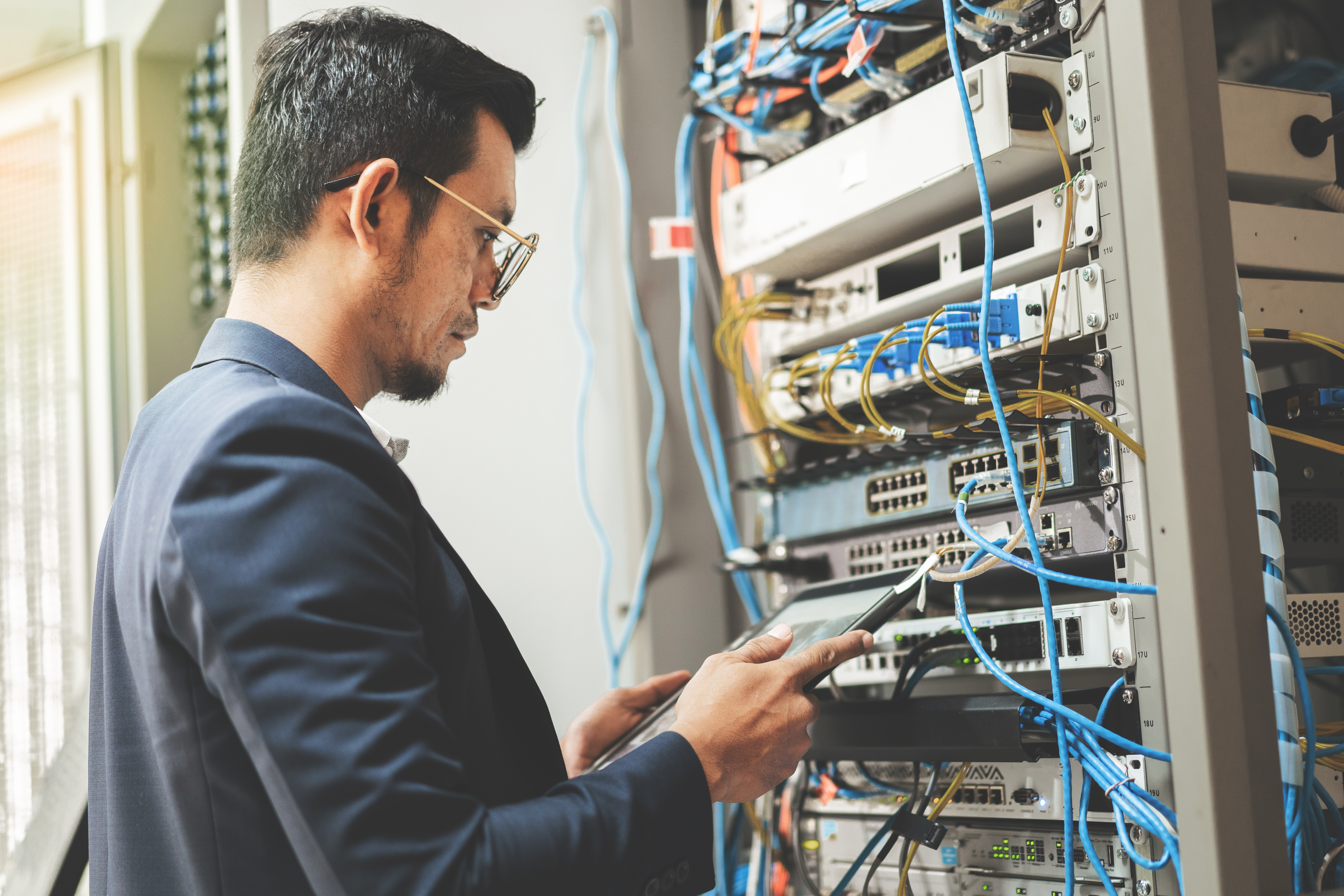 network technician holding tablet working to connecting network cables in server cabinet in network server room. IT engineer wor