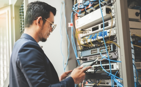 network technician holding tablet working to connecting network cables in server cabinet in network server room. IT engineer wor